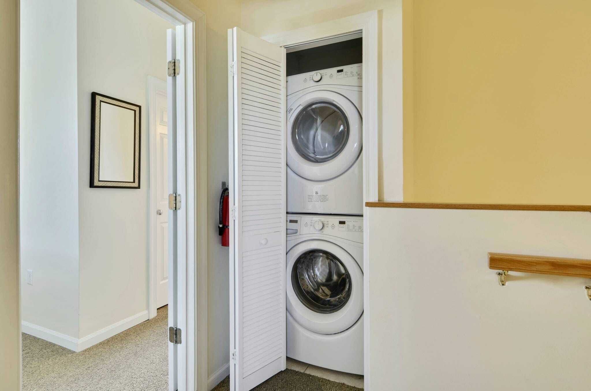 Une buanderie équipée d’un lave-linge et d’un sèche-linge à chargement frontal, d’une porte avec une poignée et d’un petit tableau encadré accroché au mur.