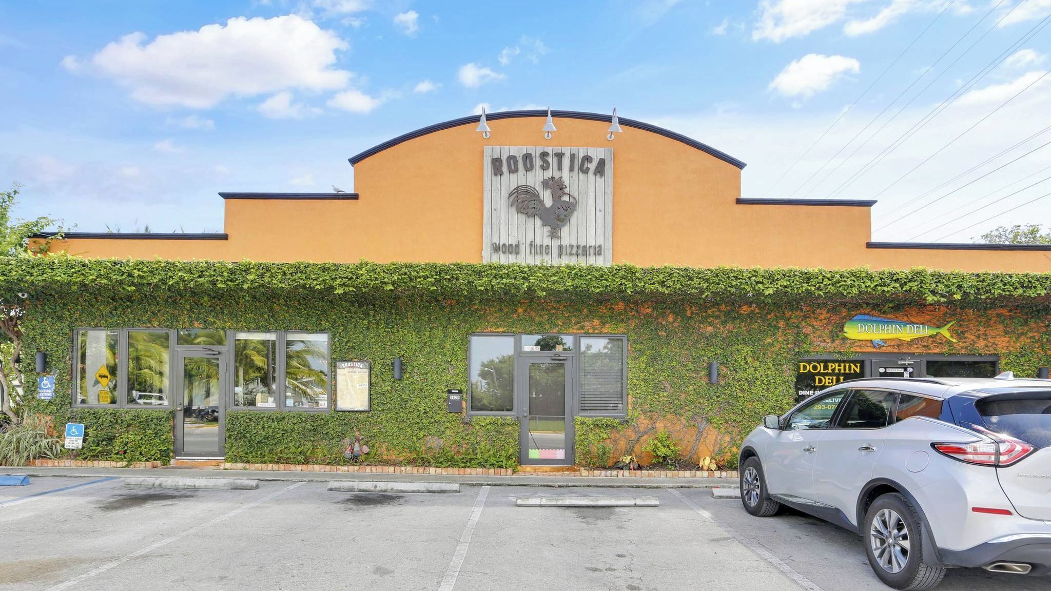 A building with a sign reading 'ROOSTICA Wood fine pizza,' a car parked in front, and a dolphin sign on the side.