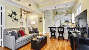 A modern living room with a grey sofa, black ottoman, and a dining area with black chairs and a black table. - Lazy Gecko by Avantstay Walk to Duval St in Key West! Month Long Stays Only (Key West)