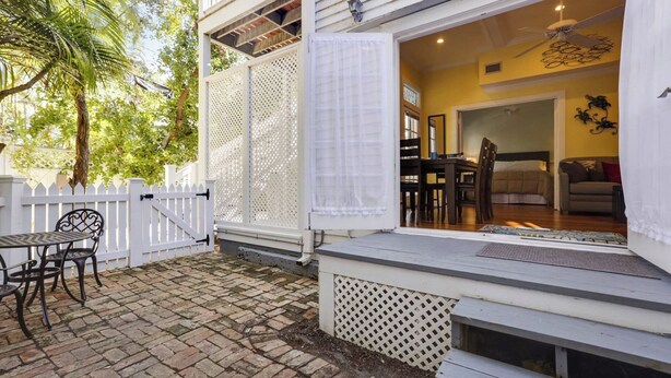 A patio with a white fence, a table and chairs, and a view into a living room with a couch and a dining table. - Lazy Gecko by Avantstay Walk to Duval St in Key West! Month Long Stays Only (Key West)