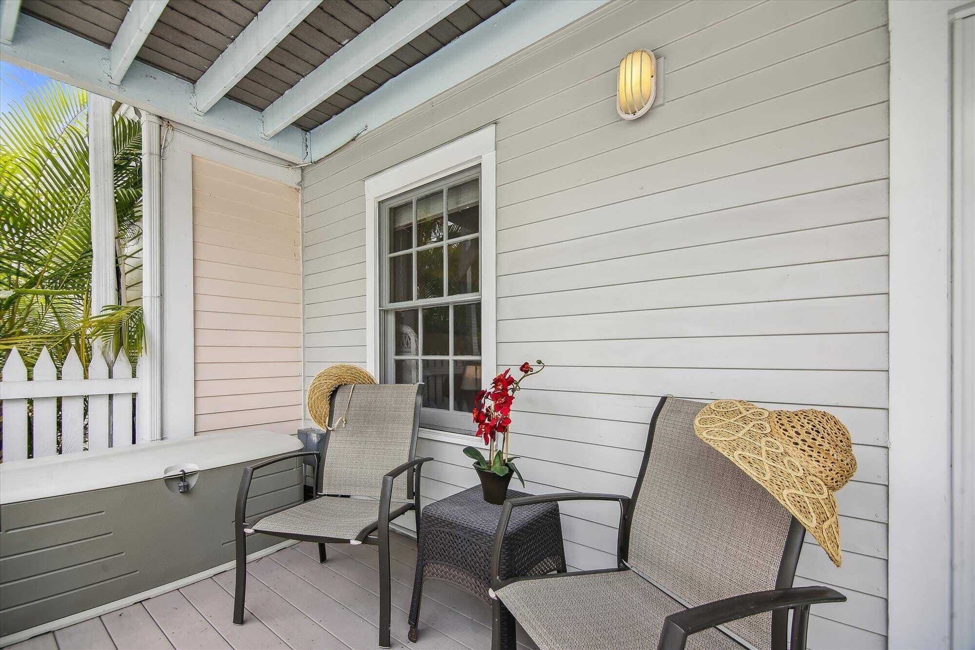 A covered porch with two wicker chairs, a small table, and a potted plant.