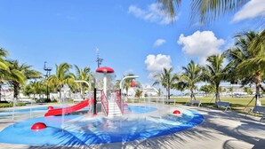 Een waterpark met glijbanen, een centraal waterattractie en palmbomen.