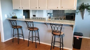 A kitchen with three bar stools, a granite countertop, white cabinets, and a trash can. - OKC - Curtis · Self Check-in-King-Fast wifi-20min 2 anywhere (Oklahoma City)