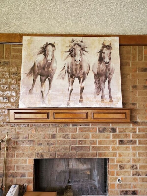 A fireplace with a large equestrian-themed painting above it.