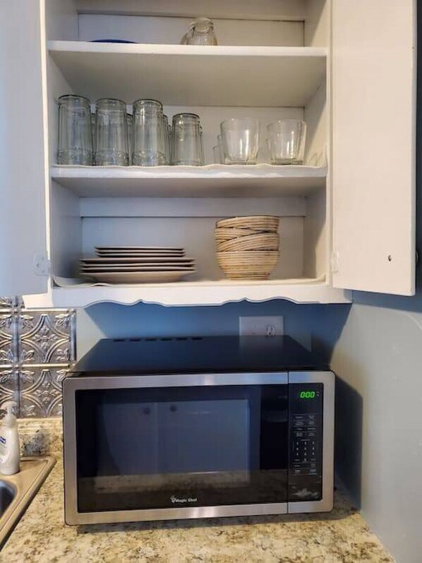 A kitchen with a microwave oven, a shelf with glass jars and plates, and a woven basket.