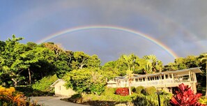 Une maison avec un jardin et un arc-en-ciel dans le ciel.