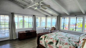 A bedroom with a bed, a desk, and a chair. There are large windows with curtains, a ceiling fan, and a view of the outdoors. - Quiet 3-bedroom house on 2.5 acres w/ocean and town views, 6 beds (Kailua-Kona)