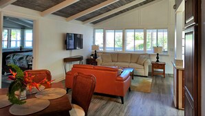 A living room with a beige sofa, orange armchair, and a dining table with a vase of flowers. - Quiet 3-bedroom house on 2.5 acres w/ocean and town views, 6 beds (Kailua-Kona)