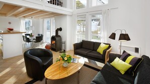 A spacious living area with a sofa, armchair, and a coffee table with flowers. There is a fireplace and a dining area with chairs and a table.