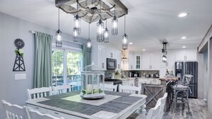 A modern kitchen with white cabinetry, a dining area with a white table and chairs, and hanging pendant lights.