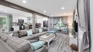 Un salón amplio con un sofá seccional gris grande, una mesa de centro y una cocina al fondo.