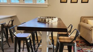 A dining area with a wooden table and chairs, a woven tray, and a view of the outside through large windows. - Walking Distance to Aggieville, K-State, and City Park! (Manhattan)