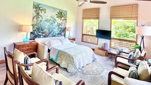 Une chambre à coucher avec un lit, des chaises en bois, un téléviseur et un tableau représentant un paysage tropical.