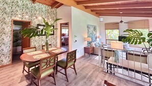 Un coin repas avec une table et des chaises en bois, une grande plante et une vue sur une chambre à coucher avec un lit et une fenêtre.