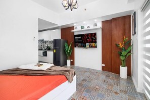 Ein modernes Schlafzimmer mit einem Bett, einem an der Wand montierten Fernseher und einer durch eine offene Tür sichtbaren Küchenzeile.