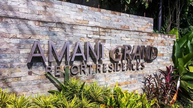 A sign for Amani Grand Resort Residences with a stone wall background and surrounding greenery. - Hyllia by J&J ( Near Airport| Wi-Fi | Netflix )  (Lapu-Lapu City)
