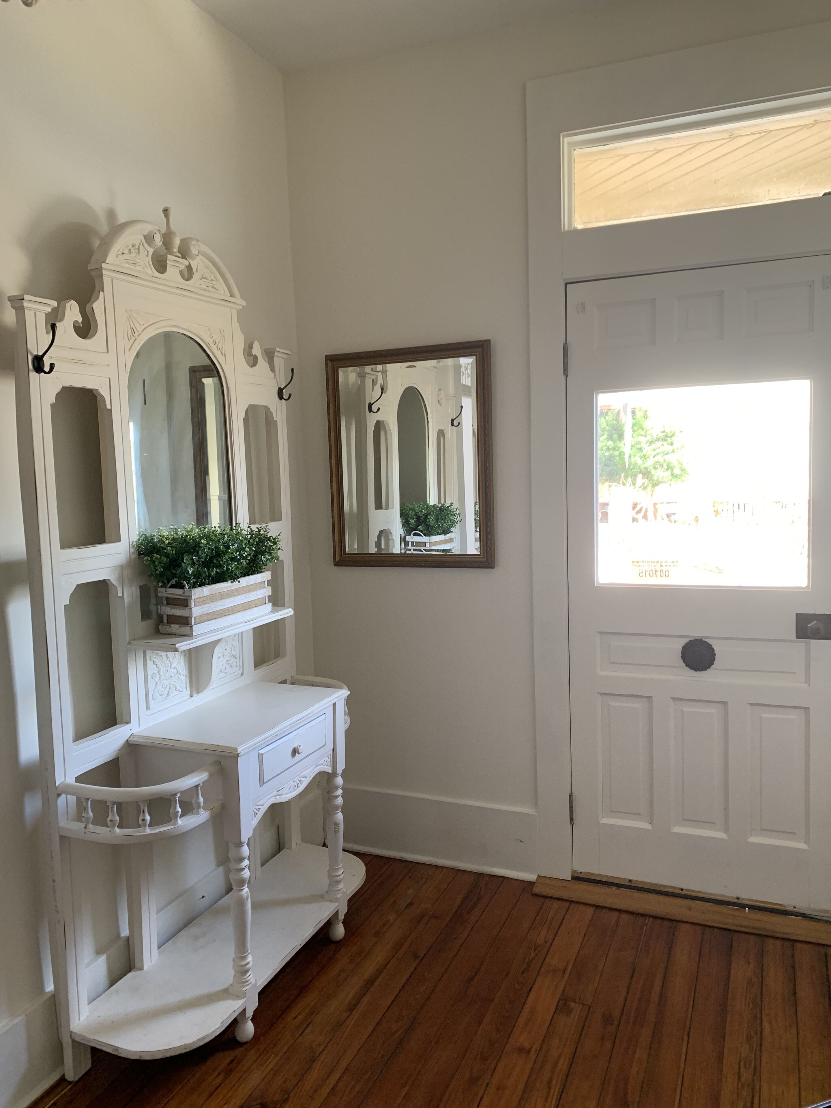A room with a white vanity, two mirrors, and a door with a window.