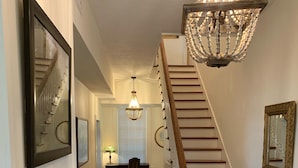 Un escalier en bois avec des balustrades blanches, un lustre et un miroir encadré.