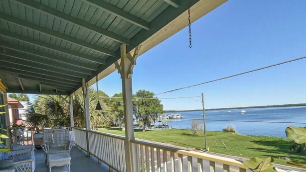 Une véranda aménagée avec du mobilier d’extérieur, une vue sur un lac et une pelouse avec des arbres.