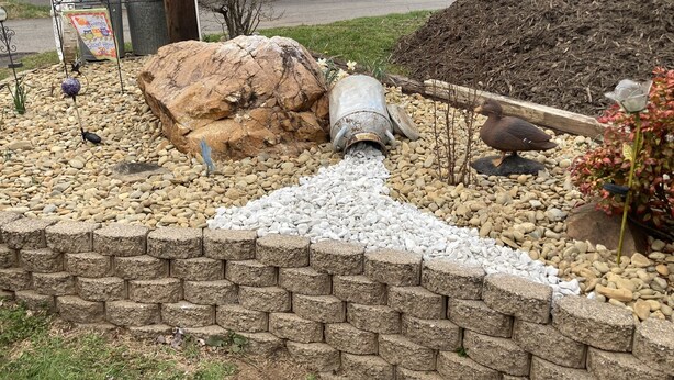 Een tuin met een betonnen pijp, rotsen en een bakstenen muur.