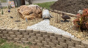 Un jardin agrémenté d’un tuyau en béton, de rochers et d’un mur en briques.