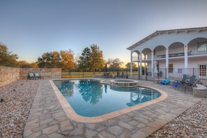 A swimming pool with a stone border, surrounded by a patio area with seating and a covered section with a railing.