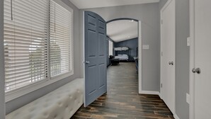 Un pasillo con un banco, una puerta que da a un dormitorio y vistas al exterior a través de persianas.