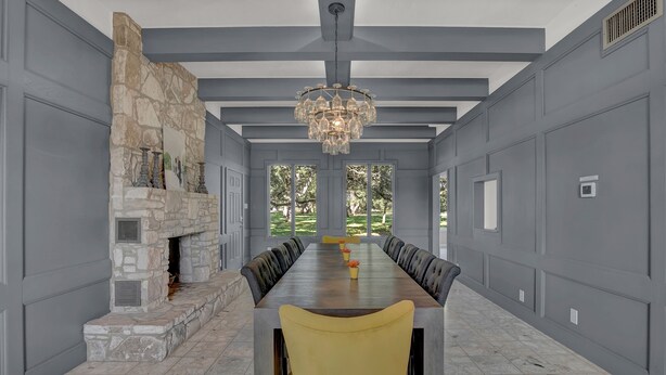 Un comedor espacioso con una mesa larga, chimenea de piedra y ventanas grandes.