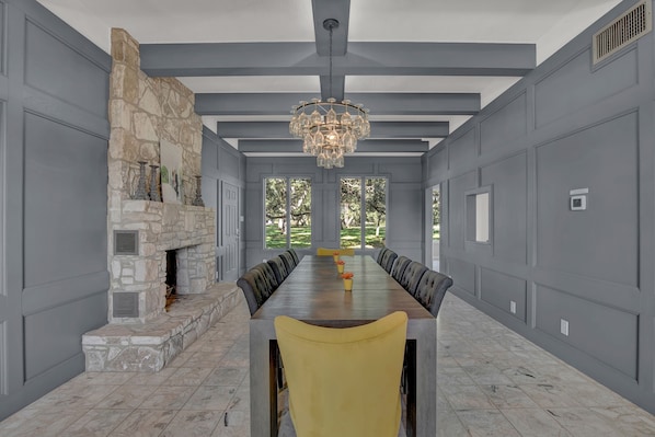 A spacious dining room with a long table, stone fireplace, and large windows.