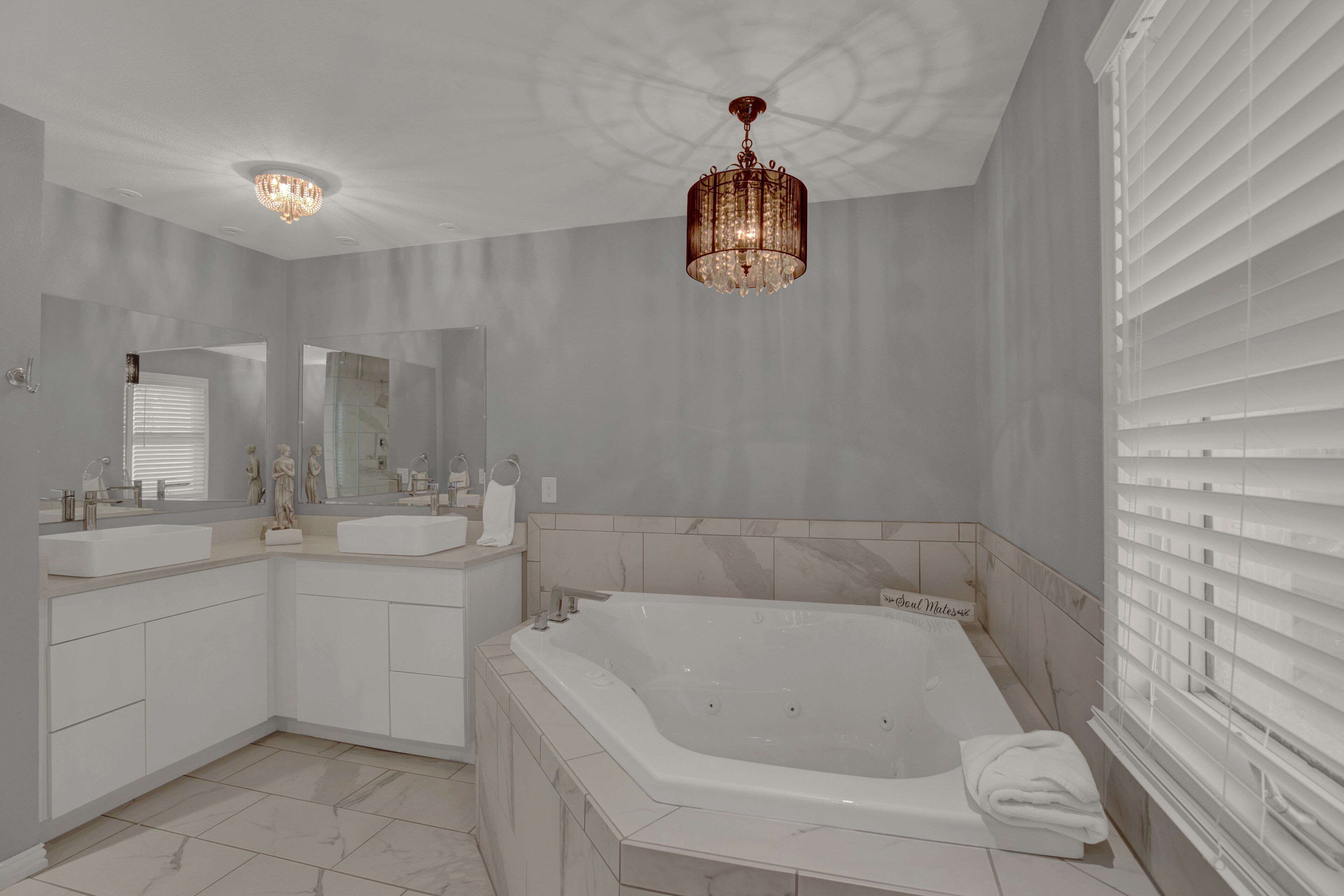 Une salle de bain moderne avec une grande baignoire, deux lavabos, un lustre et un grand miroir.