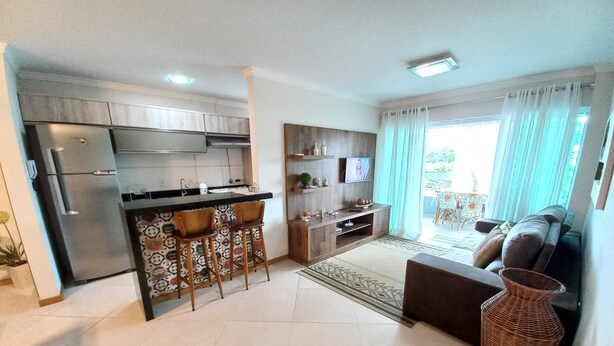 A modern kitchen with a refrigerator, bar stools, and a dining area. There is a living room with a sofa and a TV. - 314, Excelente Apartamento Para Desfrutar Férias (Bombinhas)