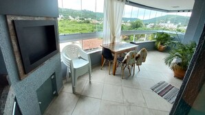 A balcony with a table and chairs, a TV, and potted plants. - 314, Excelente Apartamento Para Desfrutar Férias (Bombinhas)