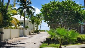 A residential street lined with palm trees and a white house with a garage. - Charming 2 bed, 2 bath cottage 100 feet from private sandy ocean beach (Islamorada)