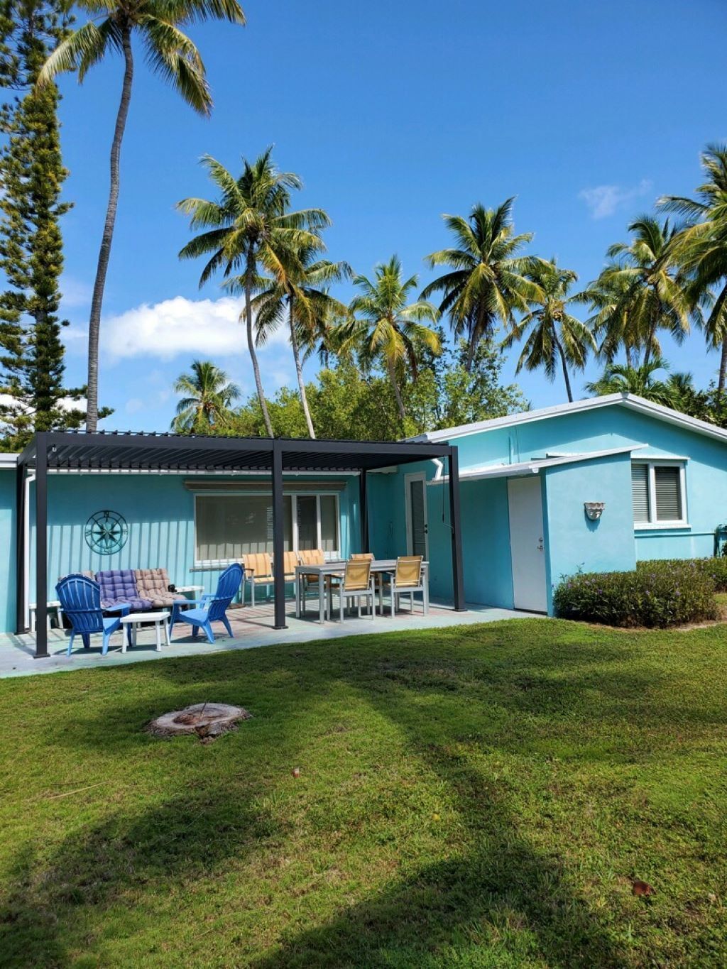 A two-story house with a covered patio area, a lawn, and palm trees in the background.