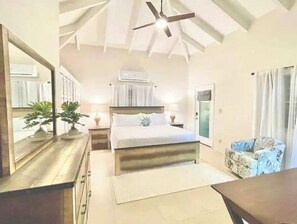 Relax in this serene bedroom with a large bed, dresser, and nightstand, complete with a ceiling fan and window with curtains.
