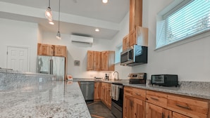 Uma cozinha moderna com bancadas de granito, armários de madeira, eletrodomésticos de aço inoxidável e uma janela grande com persianas.