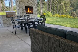 An outdoor patio with a stone fireplace, a grill, and a dining table set for six. - Water View Modern Retreat- Hot Tub + Scenic Views (Gig Harbor)
