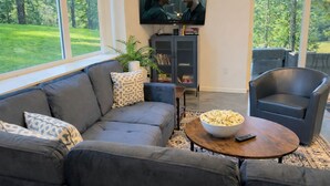 Uma sala de estar com um sofá cinzento, uma mesa de centro com uma tigela de pipoca, uma televisão na parede e uma estante de livros.