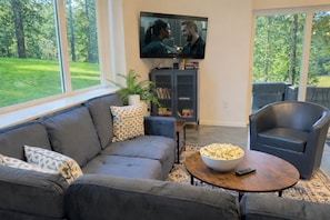 A living room with a gray sofa, a coffee table with a bowl of popcorn, a TV on the wall, and a bookshelf.