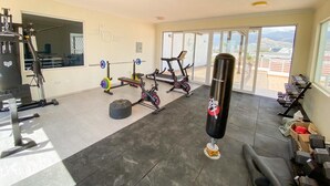 Un gimnasio con equipos de ejercicio variados, un saco de boxeo y vistas de la ciudad a través de amplias ventanas.