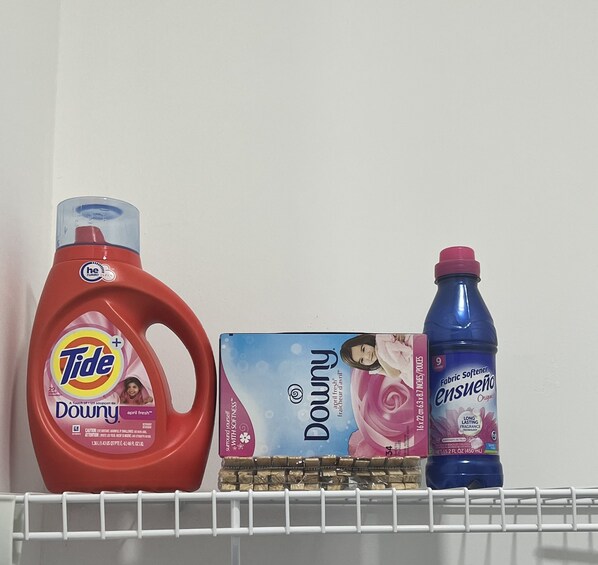 Detergente para ropa Tide Downy, una caja de suavizante Dowry y una botella de suavizante Essene sobre una estantería.
