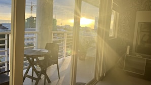 Un balcón con una mesa y sillas, un televisor y vistas a un paisaje urbano al atardecer.