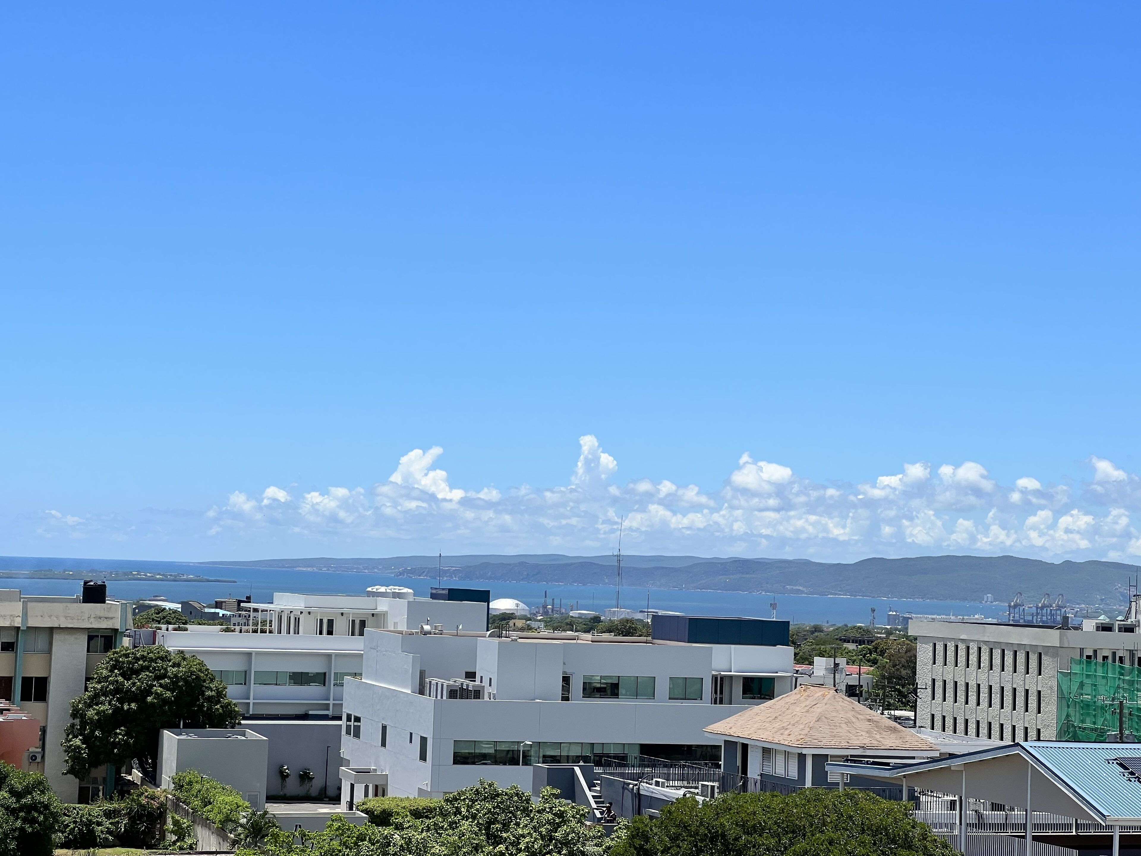 A modern urban landscape with contemporary buildings, a clear blue sky, and distant mountains.