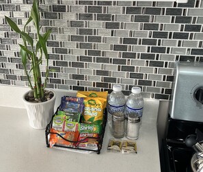A kitchen counter with a potted plant, snack bags, water bottles, and a stainless steel appliance. - Gated Luxury New Kingston 1 Bdrm Condo Pool & Gym (Kingston)