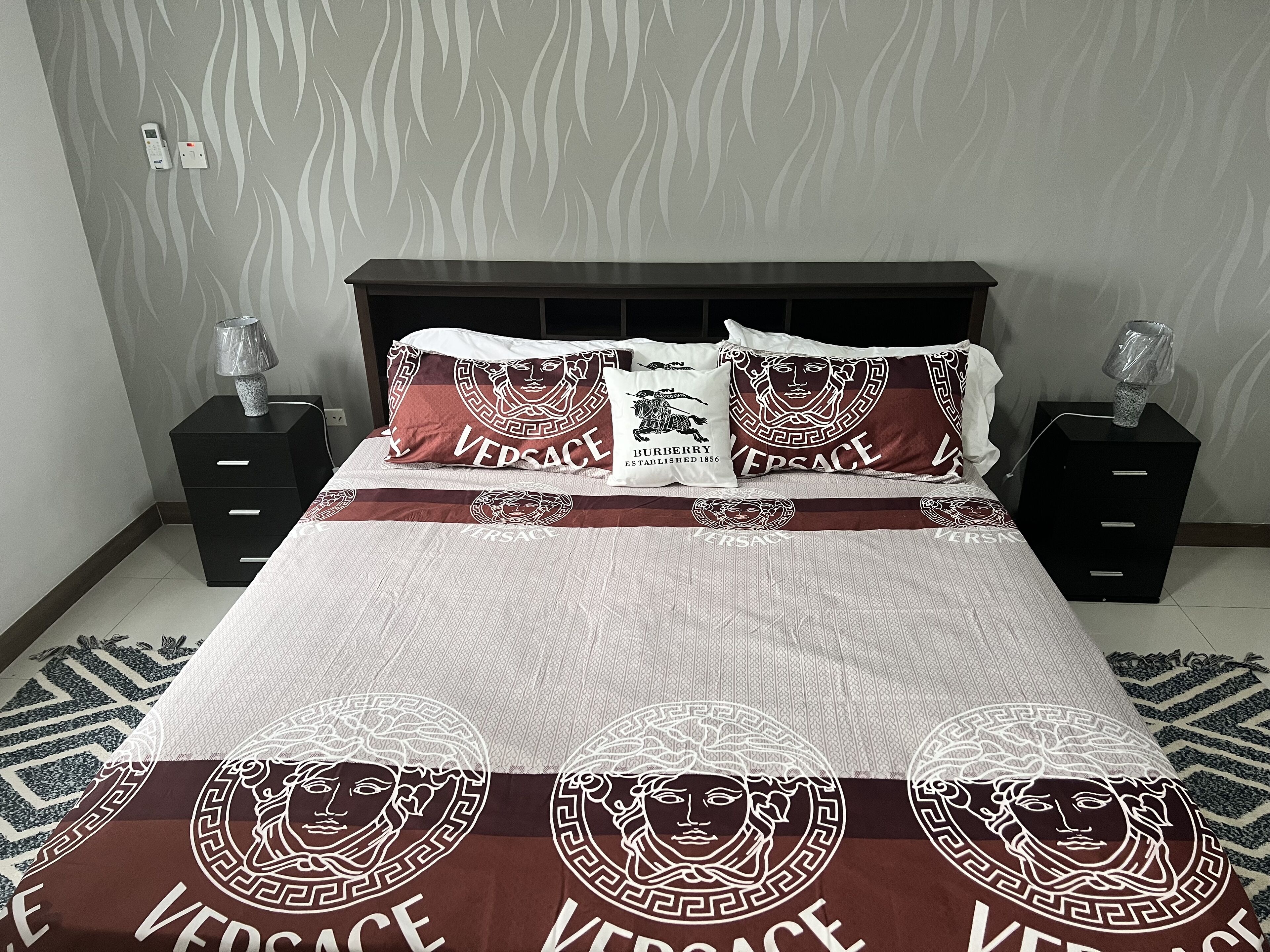 A bed with a patterned bedspread and pillows, two bedside tables with lamps, and a patterned wall.