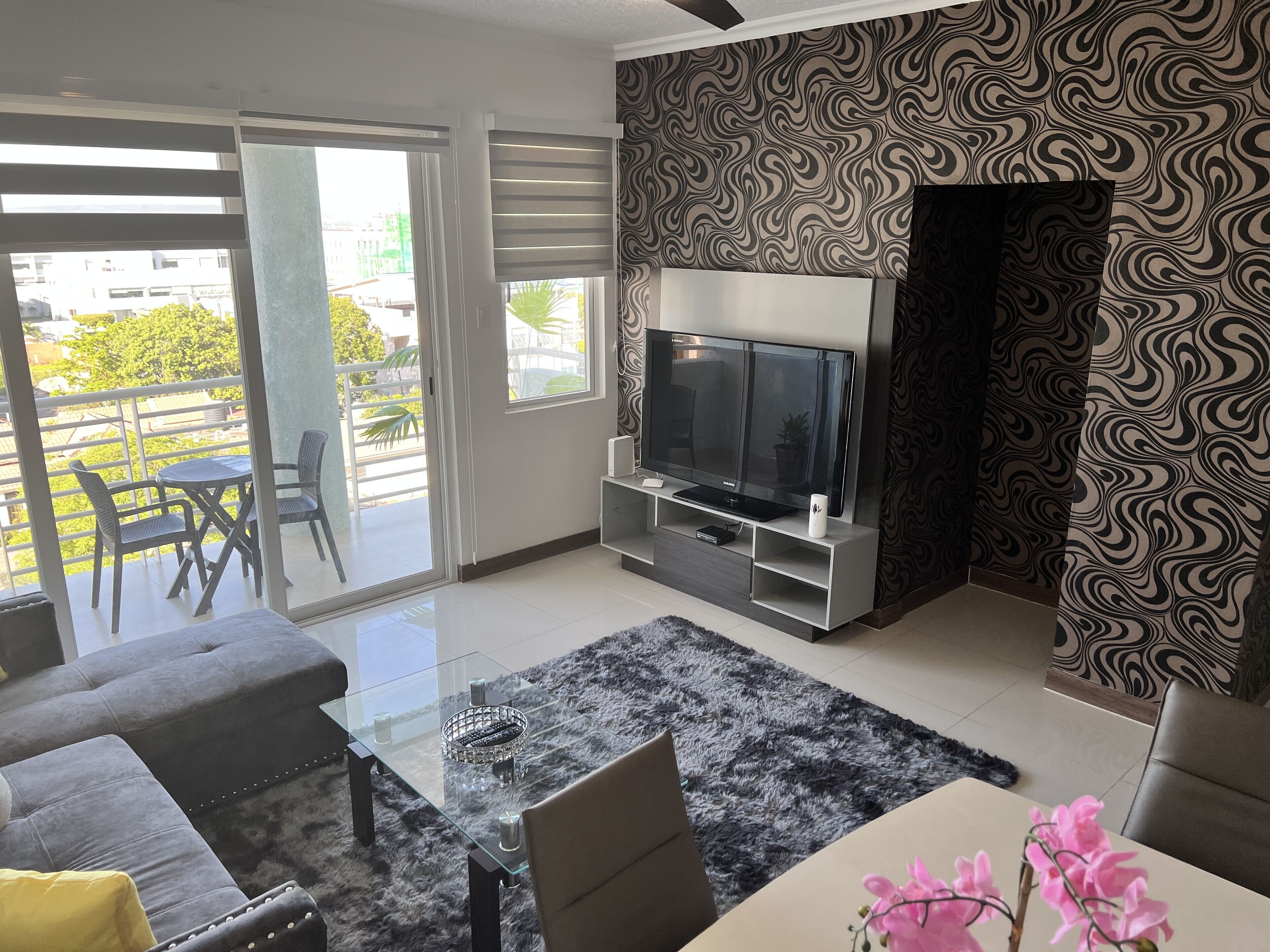 A modern living room with a flat-screen TV, a glass coffee table, and a grey sofa.