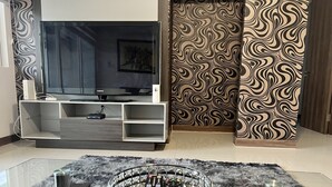 Un salón moderno con televisor de pantalla plana, una mesa de centro de vidrio y un papel tapiz estampado.