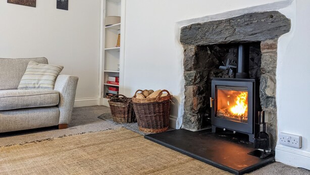 A cozy living room with a stone fireplace, a sofa, wicker baskets, and a bookshelf. - Spacious 3 bed apartment with castle view (Harlech)
