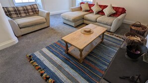 A living room with a sofa set, a coffee table, and a patterned rug. - Spacious 3 bed apartment with castle view (Harlech)