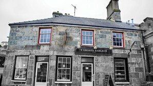 A stone building with a sign reading "Y GROSER HARLECH" and a small window display. - Spacious 3 bed apartment with castle view (Harlech)